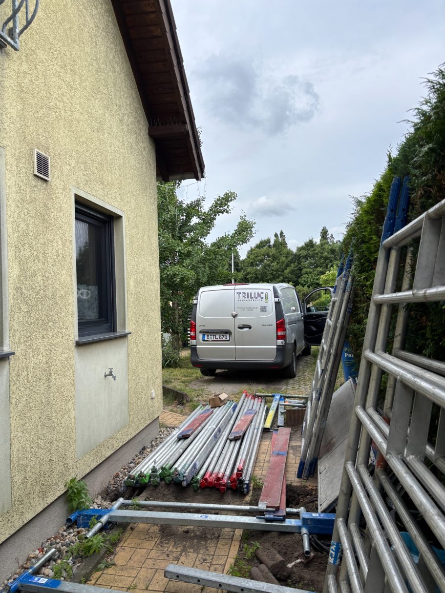 Blick auf einen Gartenweg neben einem Einfamilienhaus mit Baugeräten und Gerüst.TRILUC Servicefahrzeug im Hintergrund.