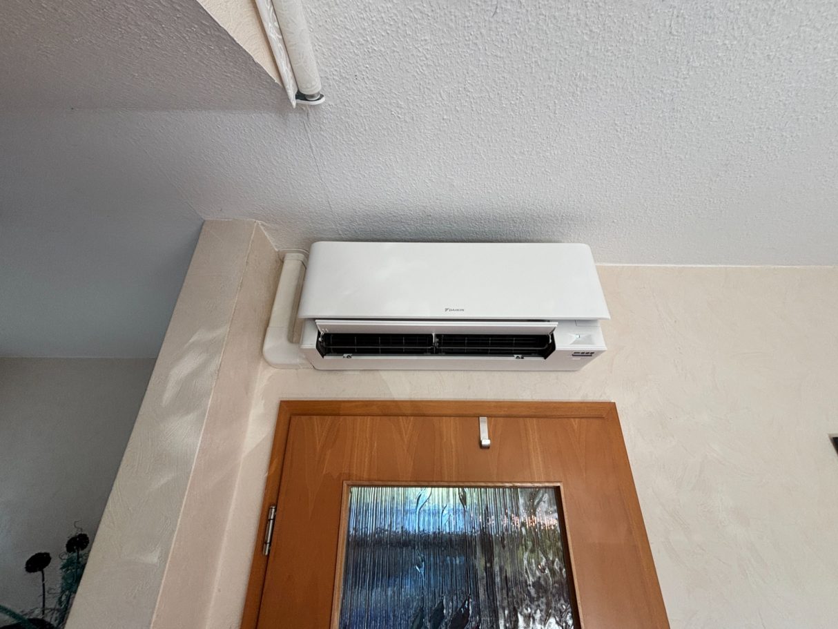 Wandmontierte Daikin Klimaanlage über einer Holztür mit Glaselement.