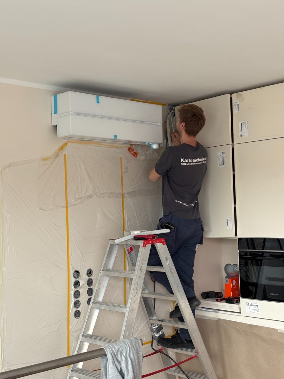 TRILUC Techniker steht auf einer Leiter und installiert eine Klimaanlage an der Küchenwand.